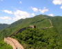 The Great Wall of China stretches across lush green mountains under a bright blue sky.