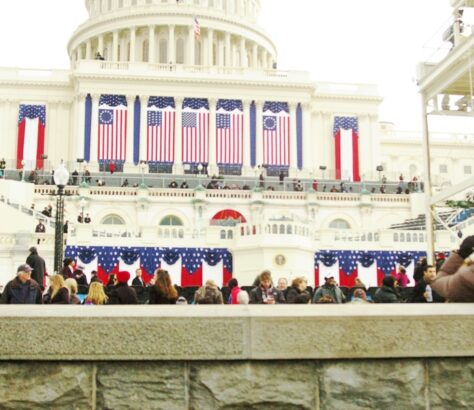 A formal event with American flags and a crowd at a government building.