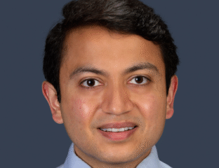 Professional headshot of a smiling man with dark hair in a light blue shirt.