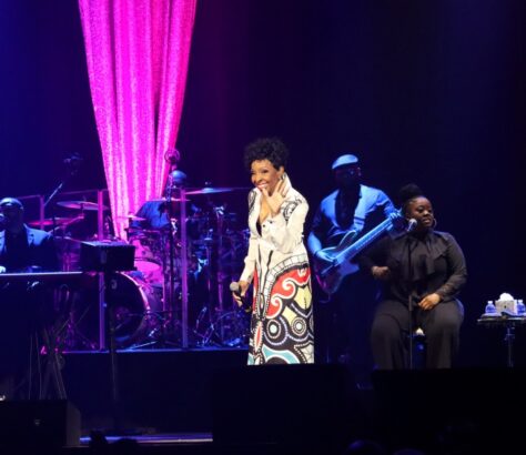 A female singer performs on stage with vibrant lighting and live band.