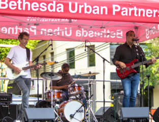 A three-member band performs live on stage at Bethesda Urban Partnership event.