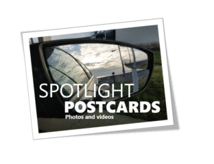 A car side mirror reflecting a cloudy road scene with text overlay about postcards.