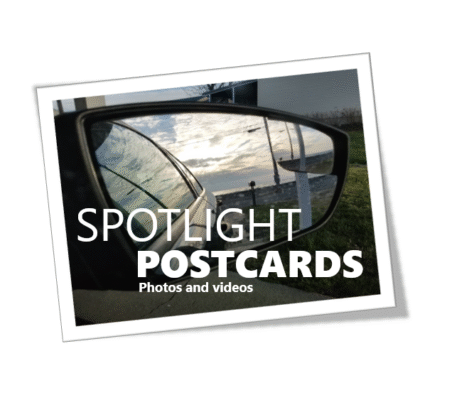 A car side mirror reflecting a cloudy road scene with text overlay about postcards.