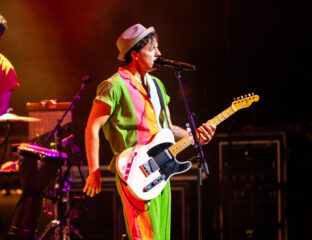 Musician passionately playing electric guitar on stage in colorful outfit.