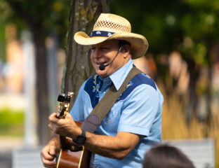 Man wearing a cowboy hat playing guitar and singing outdoors.