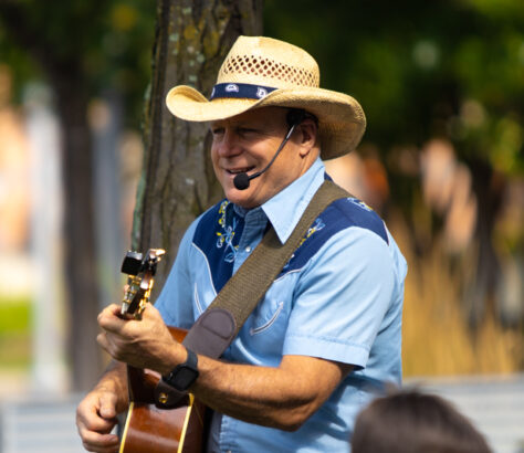 Man wearing a cowboy hat playing guitar and singing outdoors.