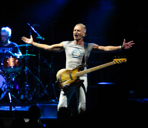 Energetic musician on stage with guitar, arms outstretched to the crowd.