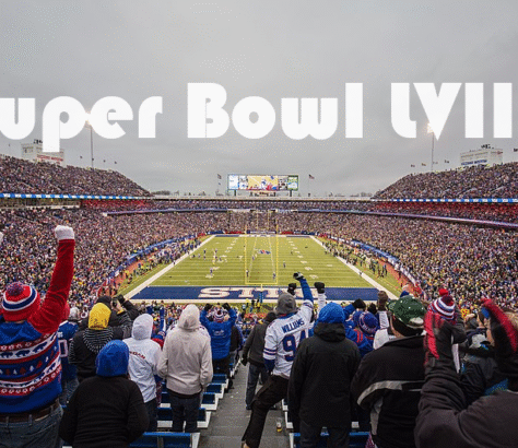Fans watch an outdoor football game in a large stadium on a cold day.