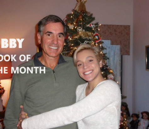 A joyful father and daughter embrace near a decorated Christmas tree.