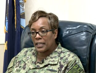 Woman in military uniform sitting on a blue leather chair.