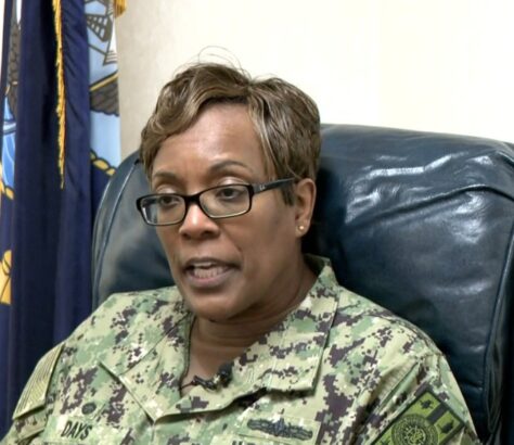 Woman in military uniform sitting on a blue leather chair.