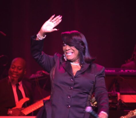 A woman joyfully waves on stage during a musical performance.