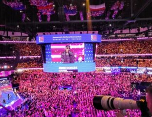 Large crowd at a concert with vibrant lighting and a big screen.