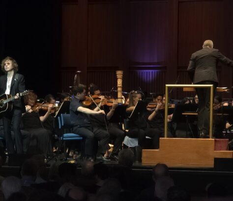 Orchestra performing live with conductor on stage.