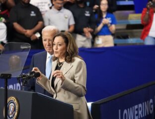 Woman speaking at a podium during an event, with a man standing behind her.