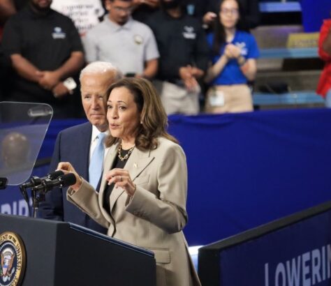 Woman speaking at a podium during an event, with a man standing behind her.