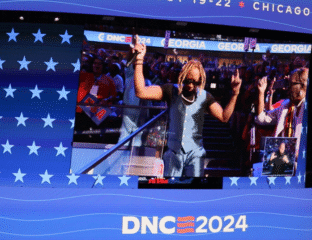 Speaker addressing crowd at DNC 2024 event with American flag backdrop.