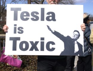 Protester holding a sign saying 'Tesla is Toxic' with a silhouette of a person.