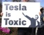 Protester holding a sign saying 'Tesla is Toxic' with a silhouette of a person.